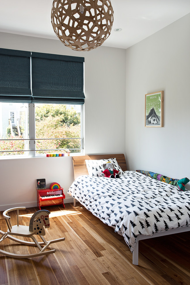 Cette photo montre une petite chambre d'enfant de 4 à 10 ans moderne avec un mur blanc, un sol en bois brun et un sol marron.