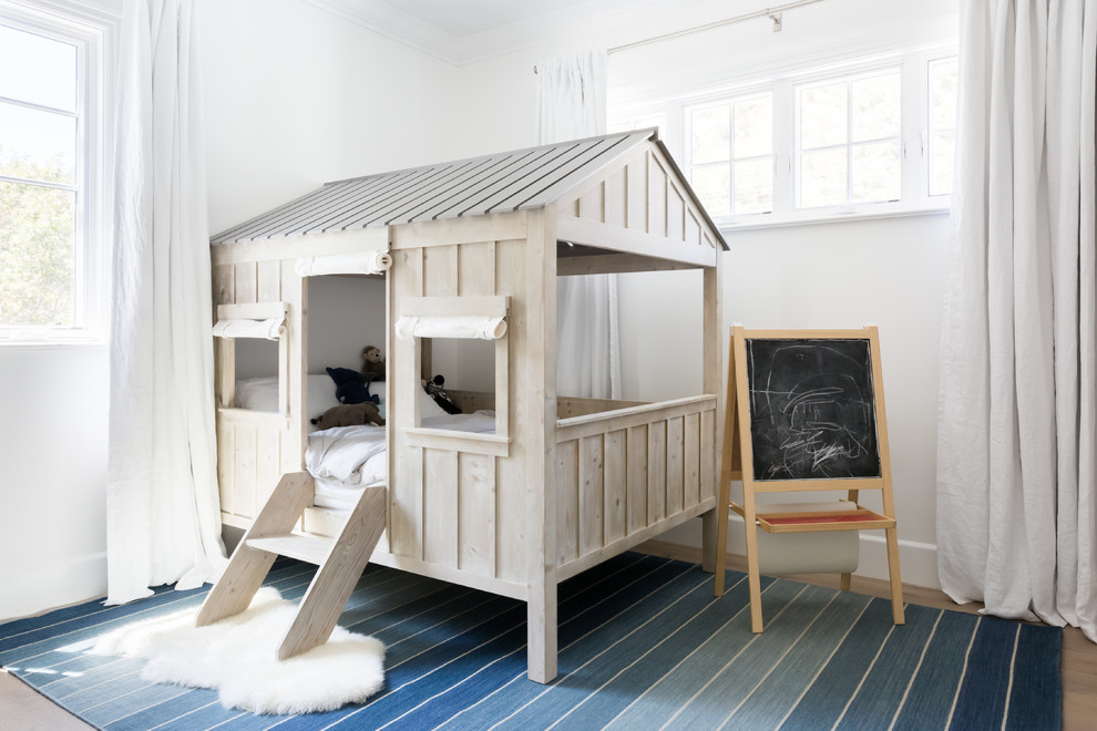 Medium sized beach style gender neutral toddler’s room in Los Angeles with white walls and light hardwood flooring.