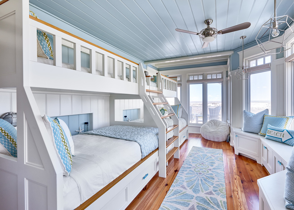 Cette photo montre une chambre d'enfant bord de mer avec un mur bleu, un sol en bois brun et un lit superposé.