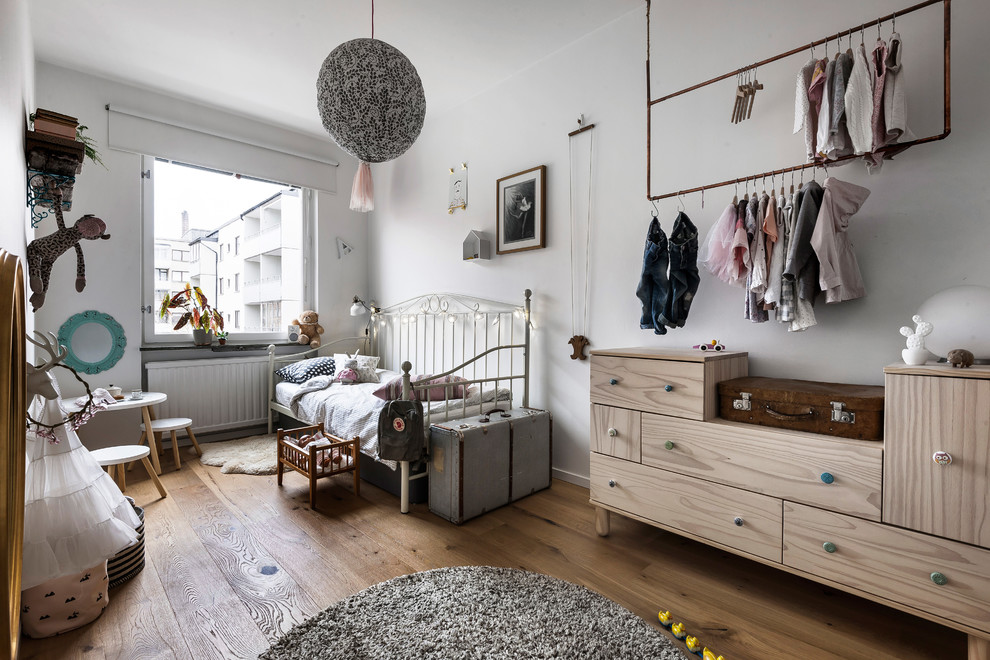 Cette image montre une chambre d'enfant nordique avec un mur blanc, un sol en bois brun et un sol marron.