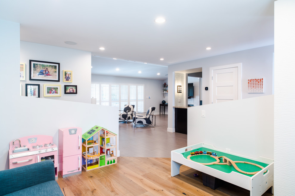 Modelo de dormitorio infantil de 4 a 10 años moderno de tamaño medio con paredes blancas, suelo de madera en tonos medios y suelo marrón