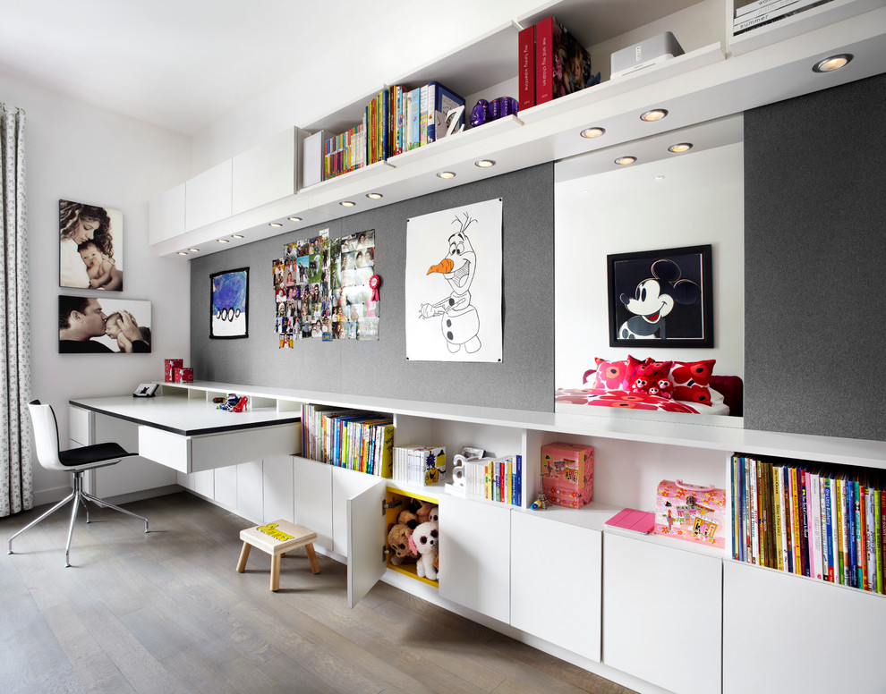 Modelo de habitación infantil unisex de 1 a 3 años contemporánea de tamaño medio con escritorio, paredes blancas y suelo de madera en tonos medios