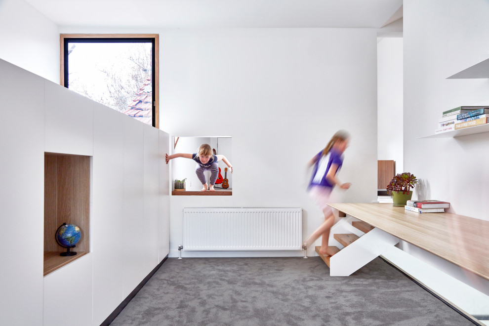 Modern inredning av ett stort barnrum kombinerat med skrivbord, med vita väggar, heltäckningsmatta och grått golv