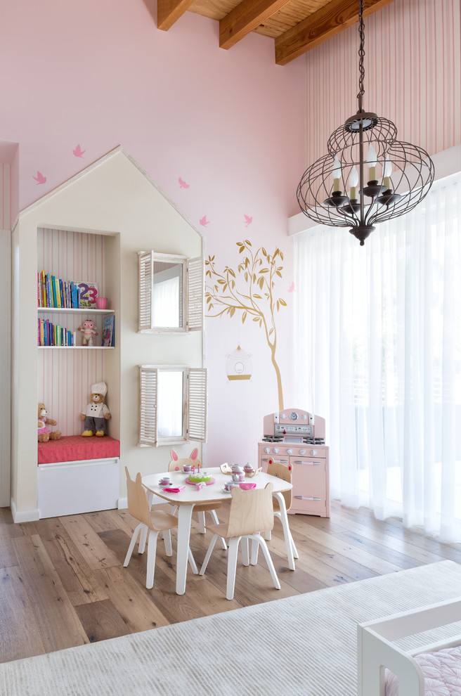 Maritim inredning av ett mellanstort barnrum kombinerat med lekrum, med rosa väggar, ljust trägolv och beiget golv