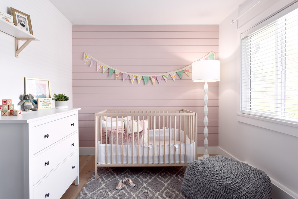 Small farmhouse nursery for girls in Vancouver with pink walls, light hardwood flooring and brown floors.