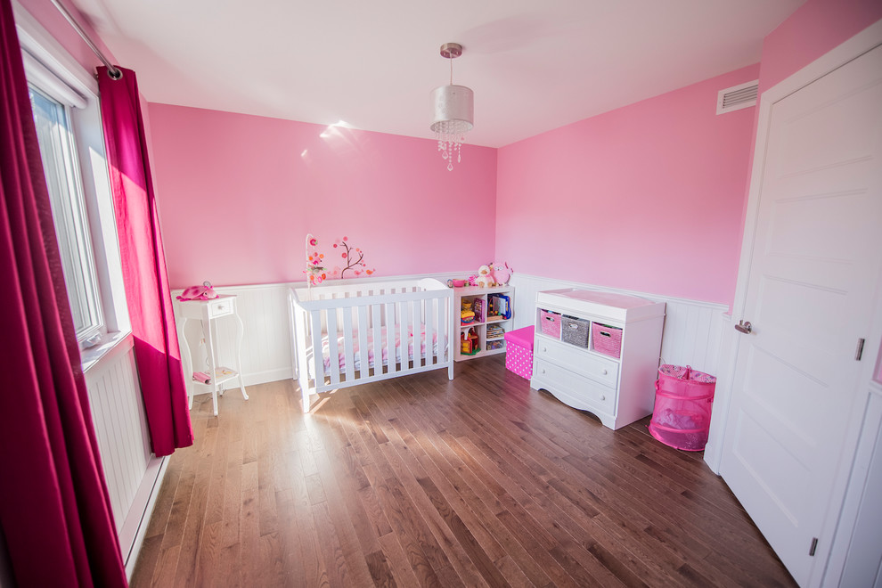 Aménagement d'une grande chambre d'enfant de 1 à 3 ans contemporaine avec un mur rose et un sol en bois brun.