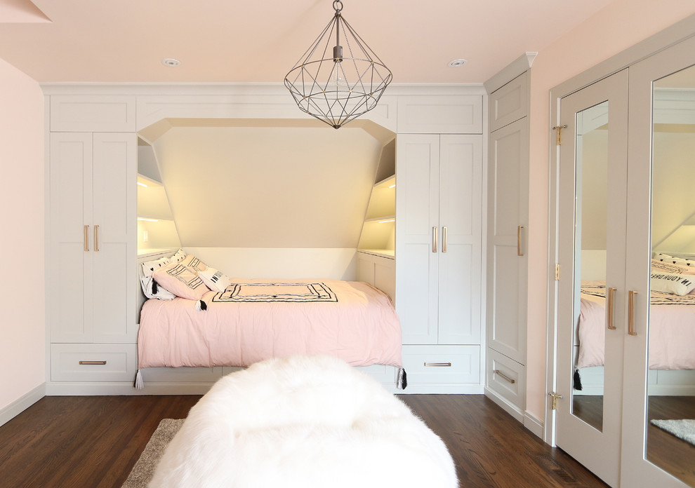 Inredning av ett klassiskt mellanstort barnrum kombinerat med sovrum, med rosa väggar, mörkt trägolv och brunt golv