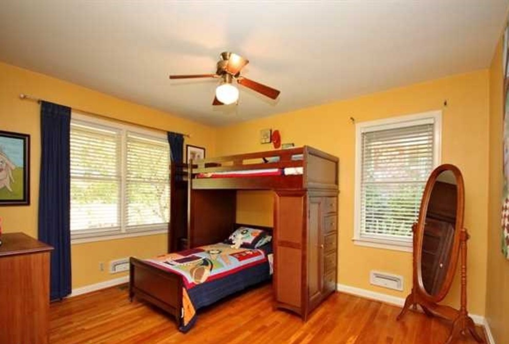 Modelo de dormitorio infantil de 4 a 10 años clásico renovado de tamaño medio con paredes amarillas y suelo de madera en tonos medios