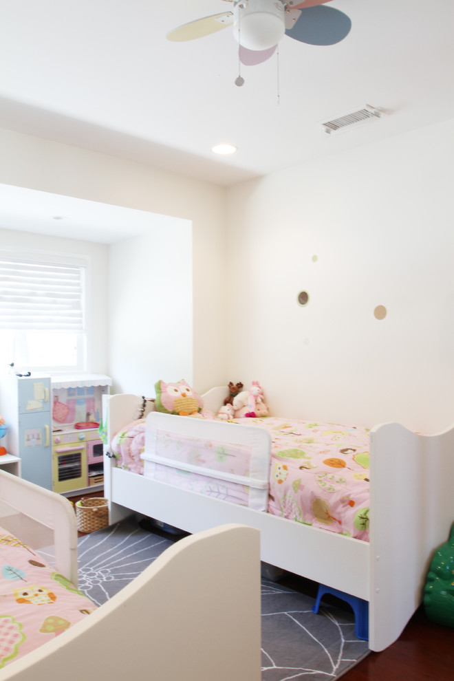 Photo of a contemporary toddler’s room for girls in Los Angeles with white walls and dark hardwood flooring.