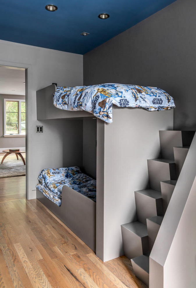 Modelo de dormitorio infantil actual con paredes grises, suelo de madera en tonos medios y suelo marrón