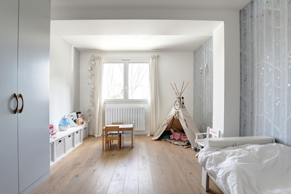 Diseño de habitación de niña de 1 a 3 años escandinava con paredes blancas, suelo de madera en tonos medios y suelo marrón