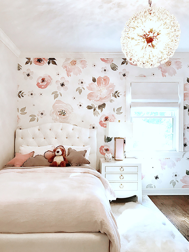 Photo of a traditional children’s room for girls in New York with pink walls, brown floors, wallpapered walls and dark hardwood flooring.