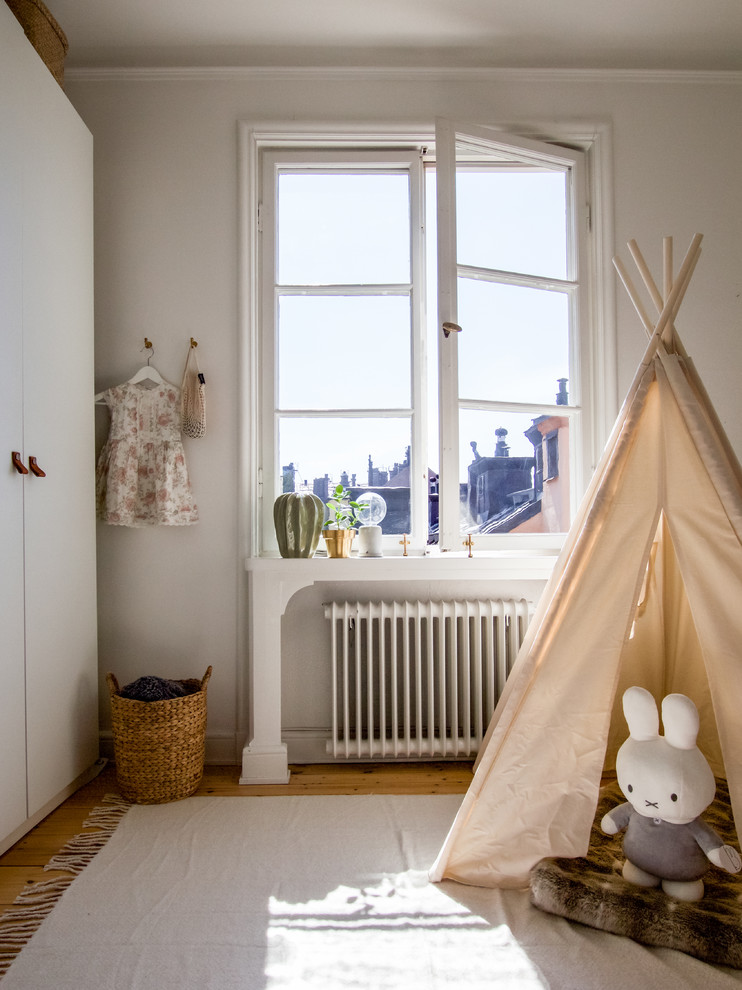 Skandinavisk inredning av ett litet barnrum kombinerat med lekrum, med vita väggar och mellanmörkt trägolv