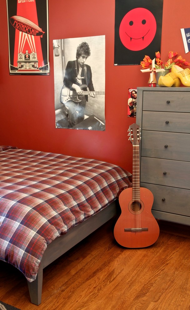 Modern inredning av ett barnrum kombinerat med sovrum, med mellanmörkt trägolv och röda väggar