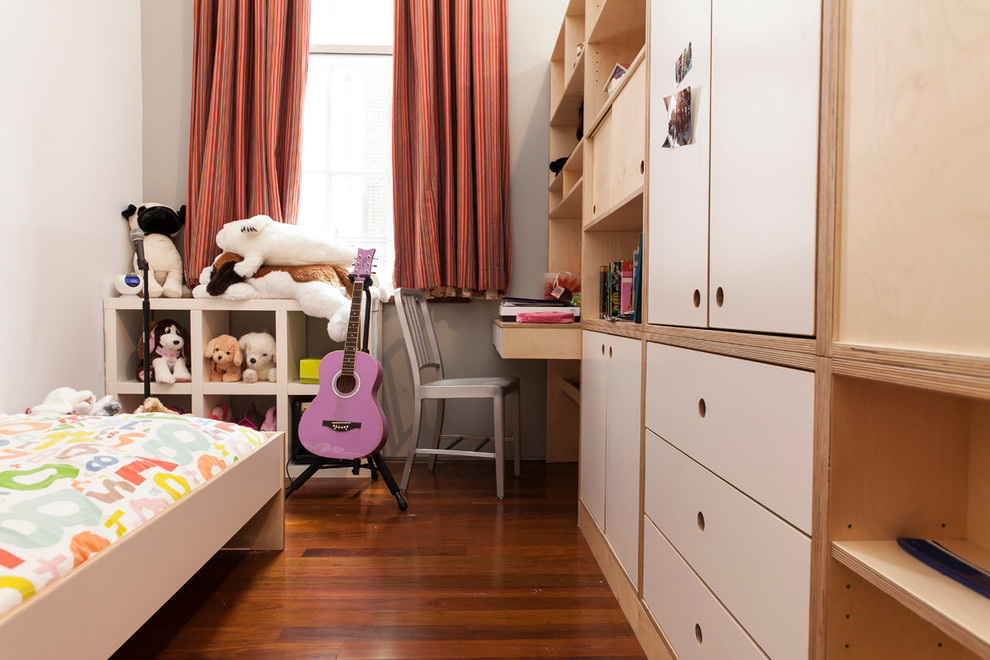 This is an example of a medium sized contemporary gender neutral children’s room in New York with white walls and medium hardwood flooring.