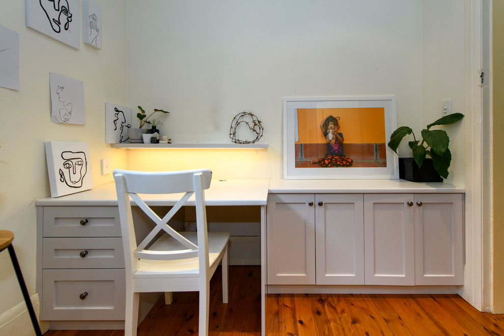 Klassisk inredning av ett litet barnrum kombinerat med skrivbord, med vita väggar och mellanmörkt trägolv