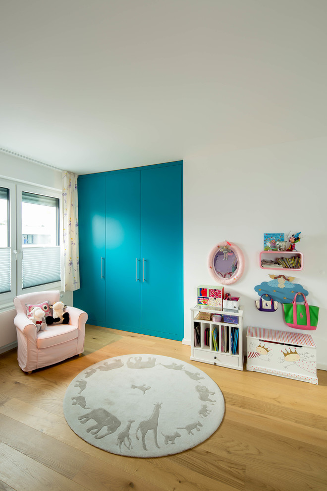 Cette image montre une grande chambre de fille de 1 à 3 ans design avec parquet clair et un mur blanc.