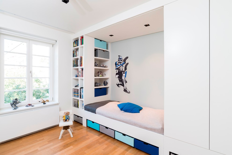 Modelo de dormitorio infantil de 4 a 10 años actual de tamaño medio con suelo de madera en tonos medios y paredes blancas