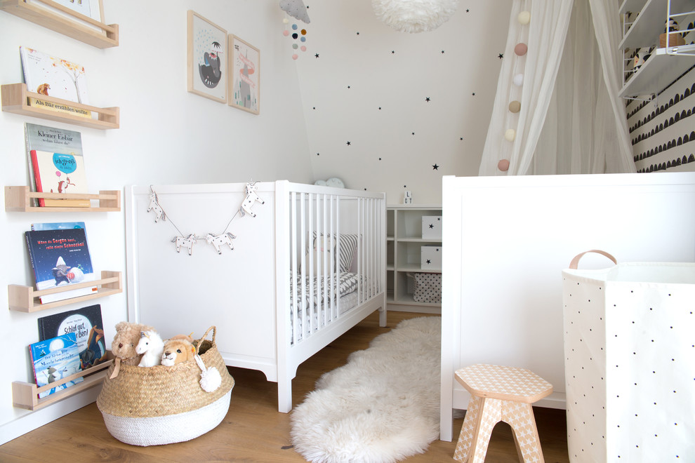 Medium sized scandinavian gender neutral nursery in Hamburg with white walls, medium hardwood flooring and brown floors.