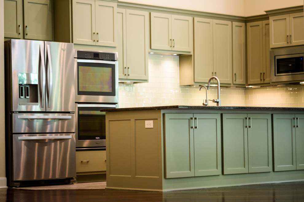 Klassisk inredning av ett mellanstort kök, med en undermonterad diskho, skåp i shakerstil, gröna skåp, granitbänkskiva, vitt stänkskydd, stänkskydd i tunnelbanekakel, rostfria vitvaror, klinkergolv i porslin och en köksö