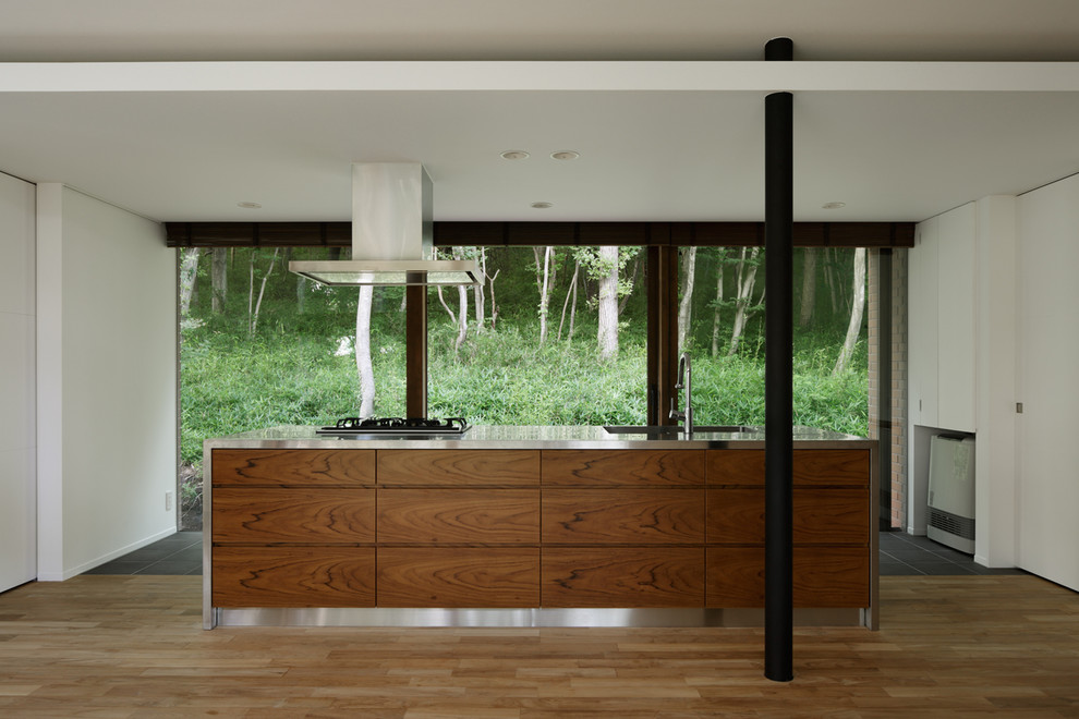 Bild på ett funkis linjärt kök med öppen planlösning, med en undermonterad diskho, luckor med profilerade fronter, skåp i mellenmörkt trä, bänkskiva i rostfritt stål, rostfria vitvaror, en köksö och ljust trägolv