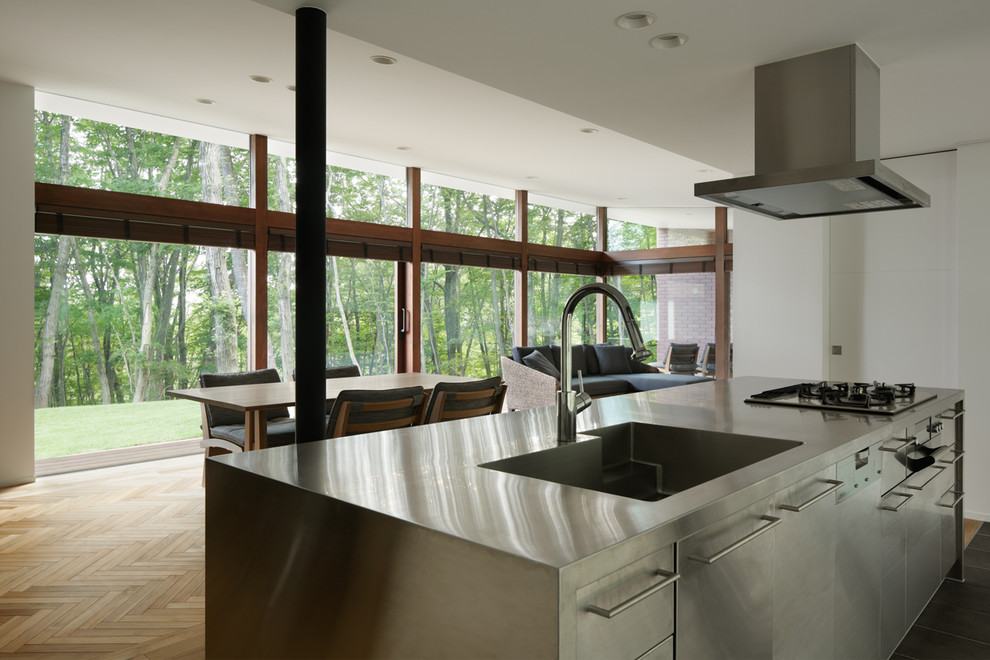 Idéer för ett modernt linjärt kök med öppen planlösning, med en undermonterad diskho, luckor med profilerade fronter, skåp i rostfritt stål, bänkskiva i rostfritt stål, rostfria vitvaror, klinkergolv i keramik, en köksö och brunt golv