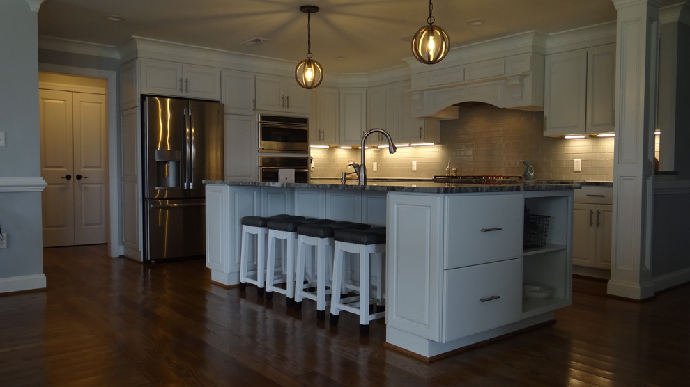 Wohnküche in L-Form mit Unterbauwaschbecken, weißen Schränken, Granit-Arbeitsplatte, Küchengeräten aus Edelstahl, braunem Holzboden und Kücheninsel in Sonstige