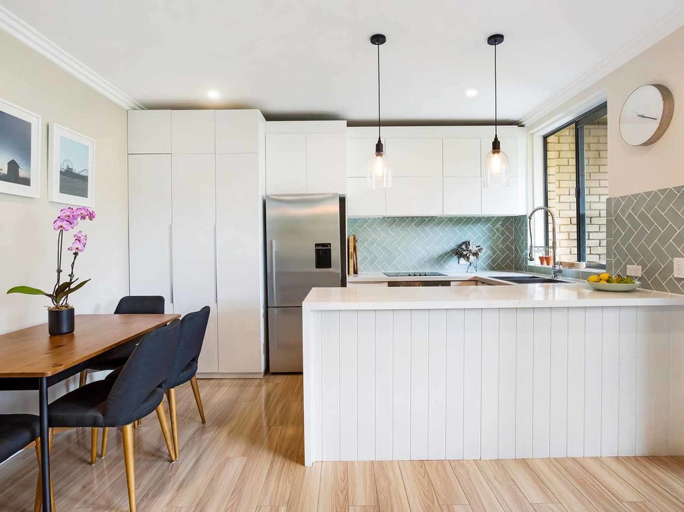 シドニーにある高級な中くらいなコンテンポラリースタイルのおしゃれなキッチン (フラットパネル扉のキャビネット、白いキャビネット、大理石カウンター、緑のキッチンパネル、シルバーの調理設備、ラミネートの床、ベージュの床、白いキッチンカウンター、ダブルシンク、窓) の写真
