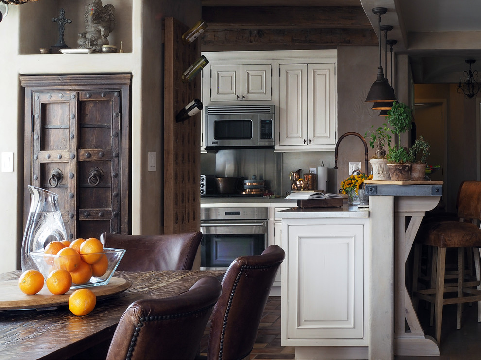 Rustik inredning av ett litet kök, med en rustik diskho, luckor med profilerade fronter, vita skåp, bänkskiva i betong, vitt stänkskydd, stänkskydd i metallkakel, rostfria vitvaror och klinkergolv i terrakotta