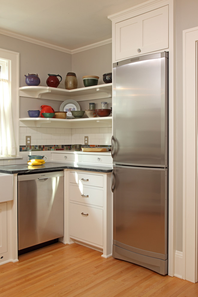 This is an example of a small traditional u-shaped enclosed kitchen in Minneapolis with a belfast sink, flat-panel cabinets, white cabinets, white splashback, metro tiled splashback, stainless steel appliances, light hardwood flooring, no island and soapstone worktops.