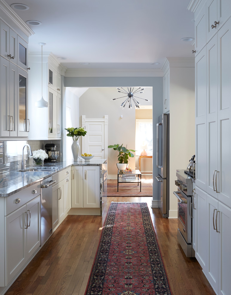 Photo of a traditional galley kitchen in Chicago with a submerged sink, shaker cabinets, white cabinets, white splashback, stainless steel appliances, medium hardwood flooring and a breakfast bar.