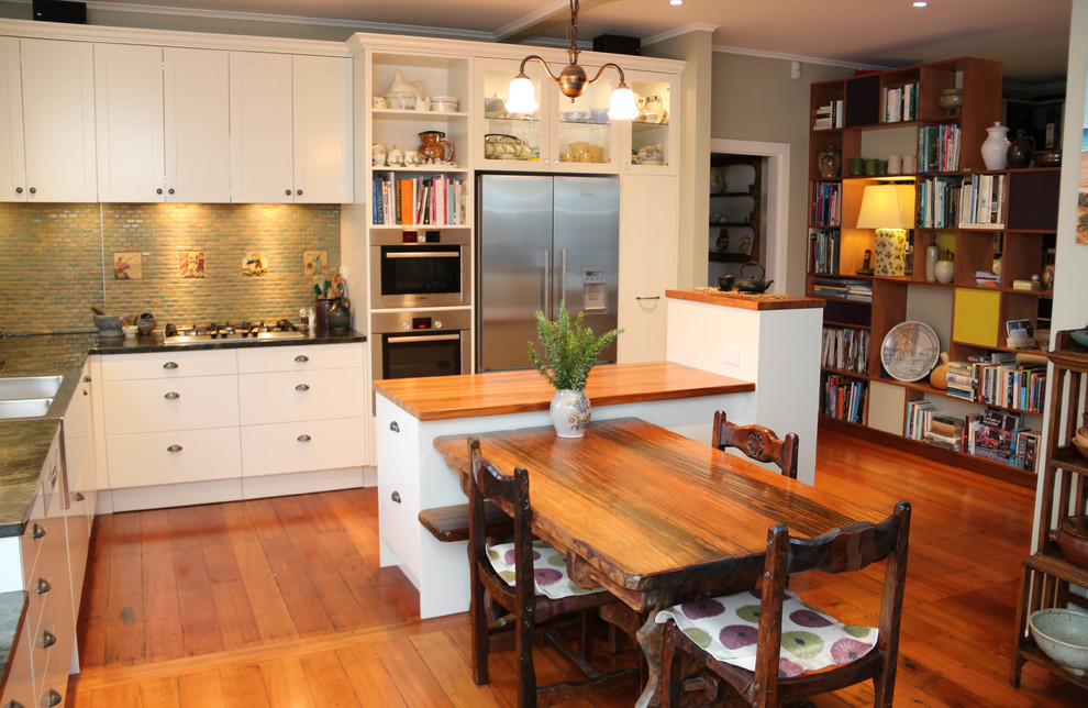 Foto på ett mellanstort vintage kök, med en dubbel diskho, vita skåp, grönt stänkskydd, stänkskydd i mosaik, rostfria vitvaror, mellanmörkt trägolv och en köksö