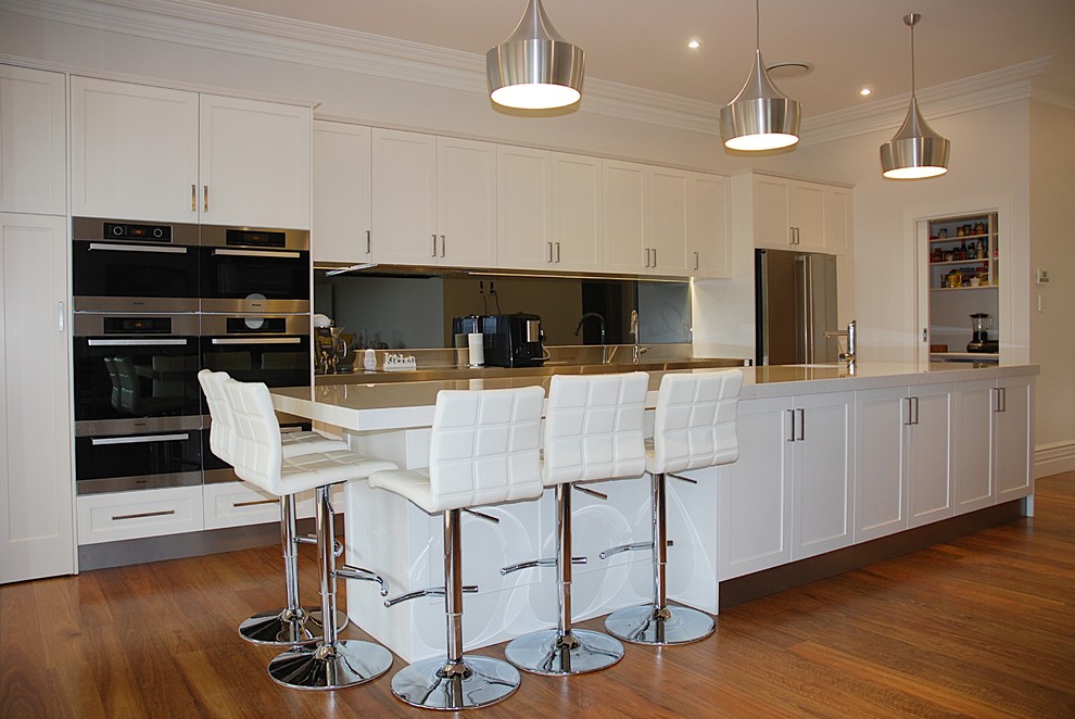 Photo of a large contemporary single-wall kitchen pantry in Sydney with a submerged sink, shaker cabinets, white cabinets, engineered stone countertops, grey splashback, stainless steel appliances, medium hardwood flooring and an island.