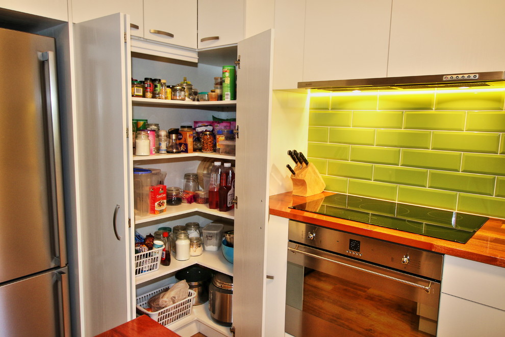 Bild på ett litet funkis kök, med en nedsänkt diskho, släta luckor, skåp i ljust trä, träbänkskiva, grönt stänkskydd, stänkskydd i tunnelbanekakel, rostfria vitvaror, ljust trägolv och en halv köksö