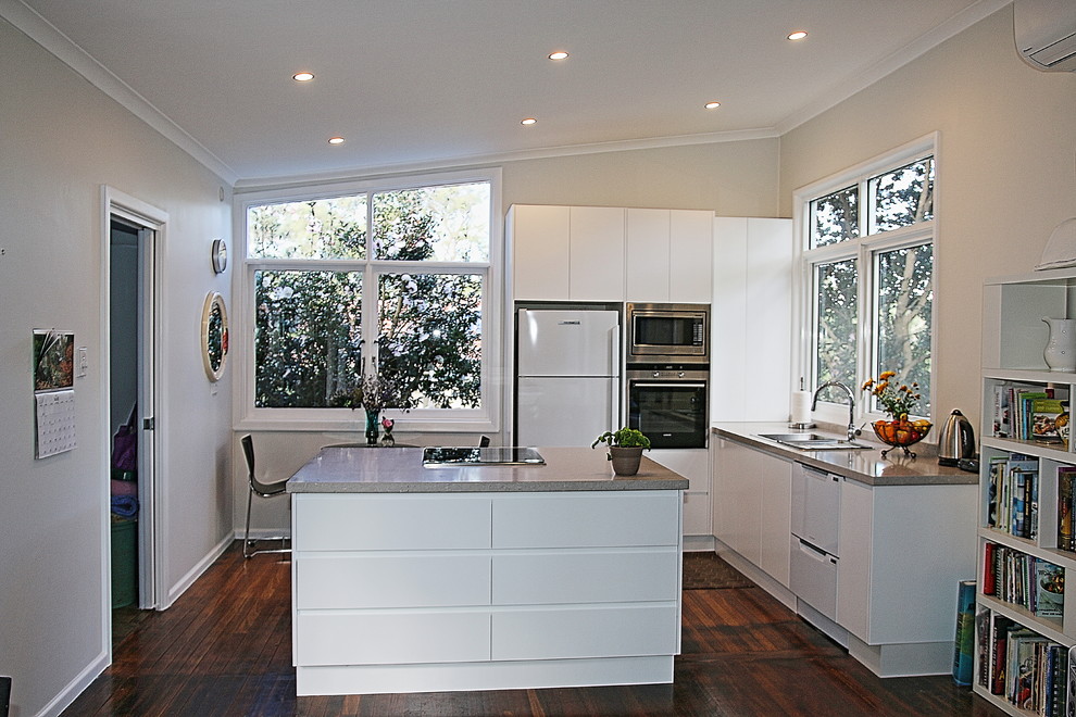 Design ideas for a small modern l-shaped kitchen/diner in Sydney with a built-in sink, flat-panel cabinets, white cabinets, engineered stone countertops, beige splashback, stone slab splashback, stainless steel appliances, medium hardwood flooring and an island.