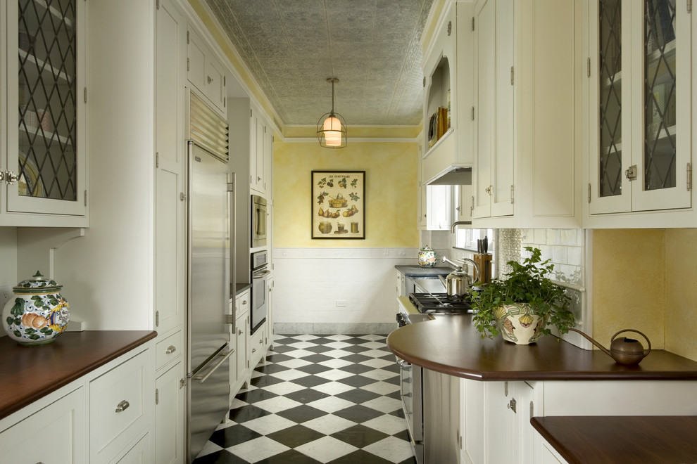 На фото: узкая отдельная, параллельная кухня в классическом стиле с стеклянными фасадами, белыми фасадами, деревянной столешницей, техникой из нержавеющей стали, полом из керамогранита и разноцветным полом без острова