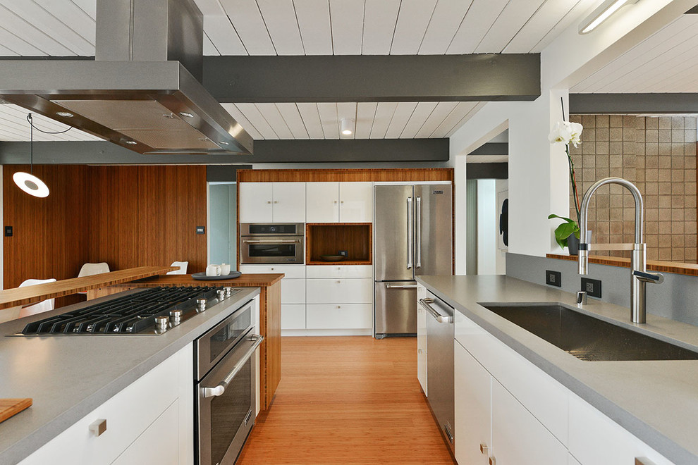 Mid-Century Küche mit Unterbauwaschbecken, flächenbündigen Schrankfronten, weißen Schränken, Küchengeräten aus Edelstahl und braunem Holzboden in San Francisco