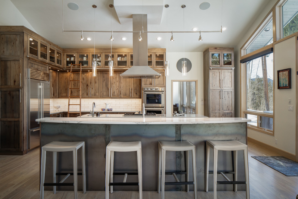 This is an example of an expansive rustic l-shaped open plan kitchen in Denver with a submerged sink, shaker cabinets, medium wood cabinets, engineered stone countertops, white splashback, metro tiled splashback, stainless steel appliances, multiple islands, brown floors, medium hardwood flooring and white worktops.