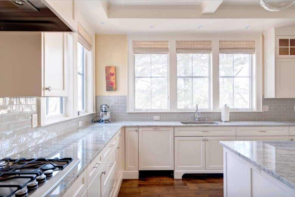 Exempel på ett stort klassiskt kök, med en nedsänkt diskho, luckor med infälld panel, vita skåp, bänkskiva i kvarts, stänkskydd i glaskakel, rostfria vitvaror, mellanmörkt trägolv och en köksö