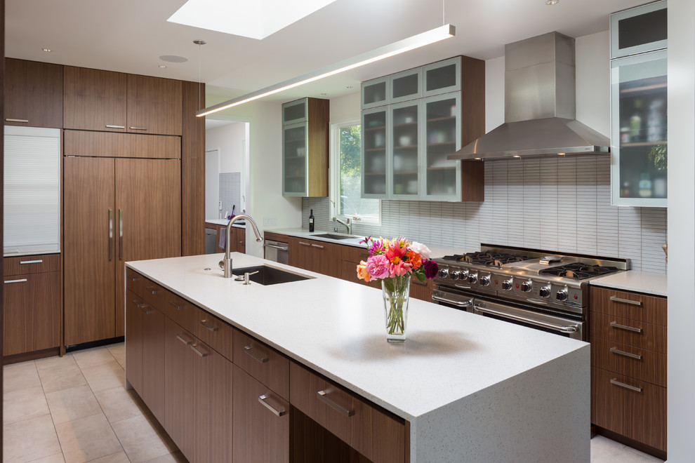 Immagine di un cucina con isola centrale minimalista con lavello sottopiano, ante lisce, ante in legno bruno, paraspruzzi bianco e elettrodomestici in acciaio inossidabile