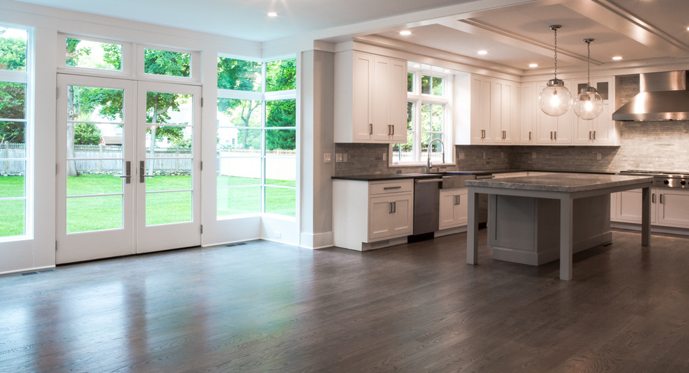 Example of a large trendy u-shaped medium tone wood floor eat-in kitchen design in New York with a farmhouse sink, flat-panel cabinets, white cabinets, granite countertops, gray backsplash, stone tile backsplash, stainless steel appliances and an island