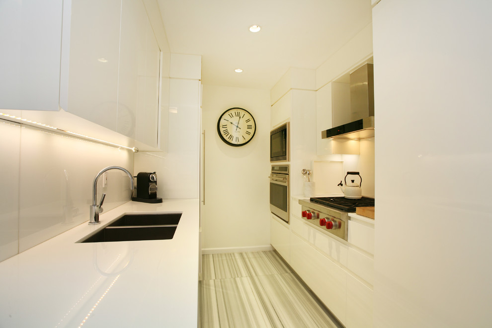 Пример оригинального дизайна: параллельная, отдельная кухня в стиле модернизм с двойной мойкой, белыми фасадами, плоскими фасадами, белым фартуком и фартуком из стекла