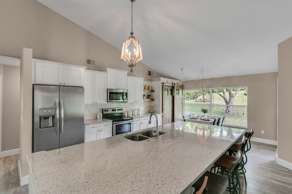 Bild på ett mellanstort lantligt grå linjärt grått kök och matrum, med en undermonterad diskho, skåp i shakerstil, vita skåp, bänkskiva i kvartsit, vitt stänkskydd, stänkskydd i keramik, rostfria vitvaror, laminatgolv, en köksö och grått golv