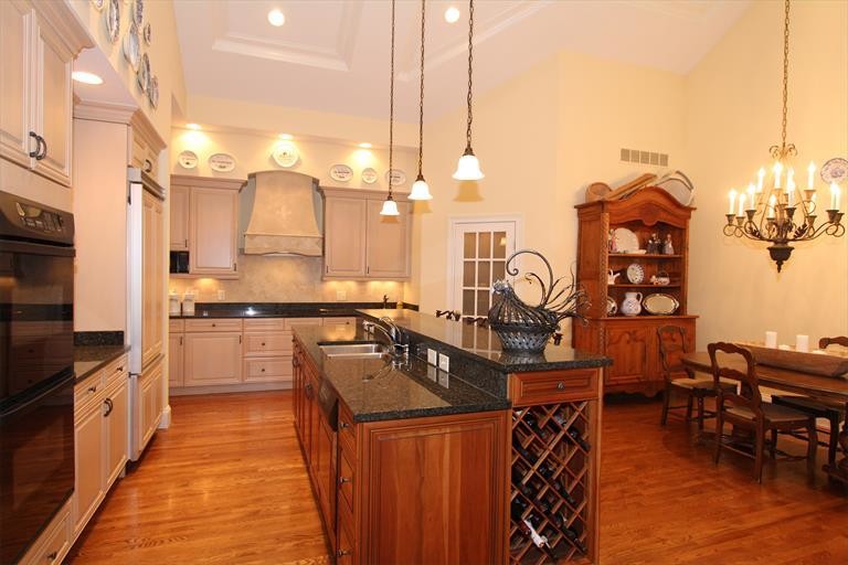 Klassisk inredning av ett mellanstort kök med öppen planlösning, med en undermonterad diskho, granitbänkskiva, beige stänkskydd, stänkskydd i keramik, svarta vitvaror, mellanmörkt trägolv och en köksö