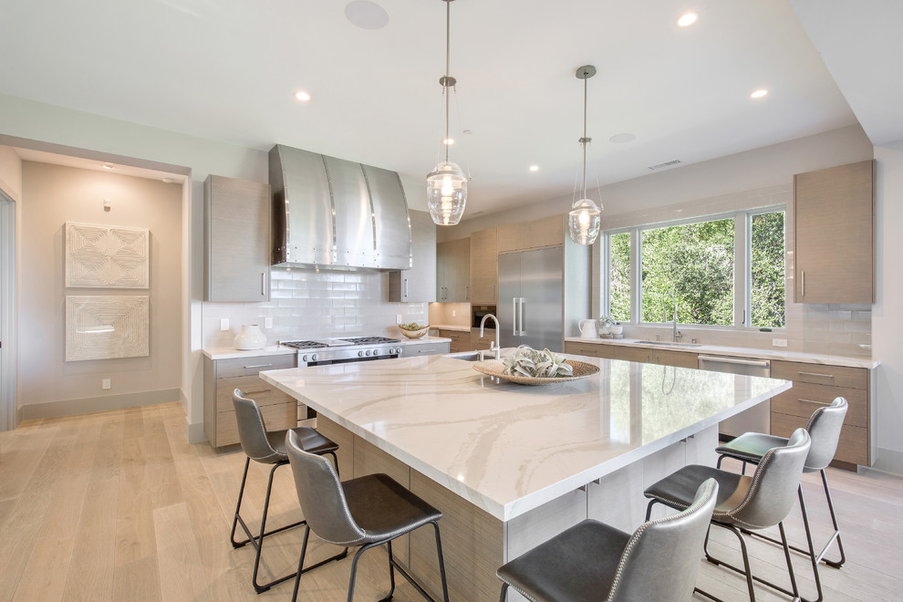 Contemporary kitchen in San Francisco with light wood cabinets, an island, a submerged sink, white splashback, metro tiled splashback, stainless steel appliances, light hardwood flooring and white worktops.