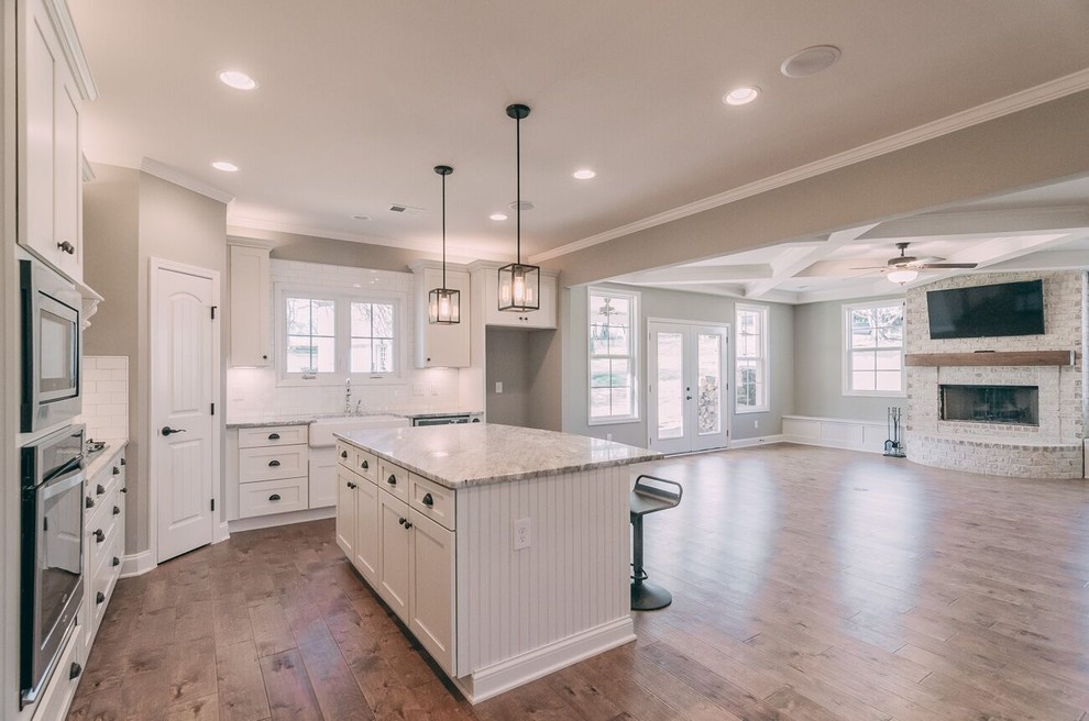 Eat-in kitchen - farmhouse l-shaped medium tone wood floor eat-in kitchen idea in Nashville with a farmhouse sink, recessed-panel cabinets, white cabinets, granite countertops, white backsplash, subway tile backsplash, stainless steel appliances and an island