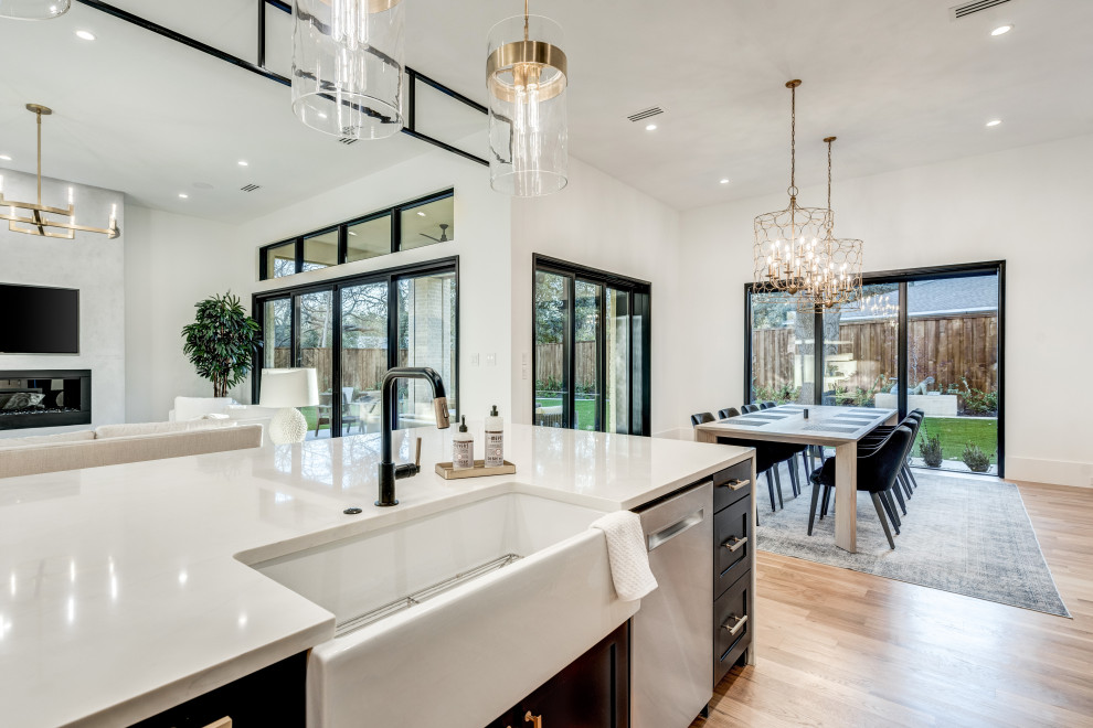 Inspiration for a modern l-shaped open plan kitchen in Dallas with a belfast sink, recessed-panel cabinets, black cabinets, engineered stone countertops, white splashback, marble splashback, stainless steel appliances, light hardwood flooring, an island, brown floors and white worktops.