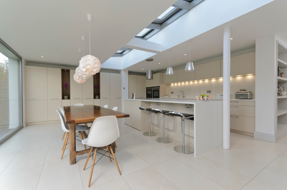 Стильный дизайн: параллельная кухня в современном стиле с обеденным столом, плоскими фасадами, бежевыми фасадами и белым полом - последний тренд