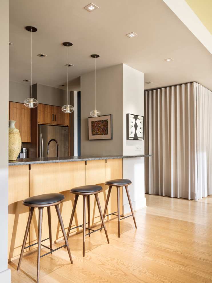 Cette photo montre une cuisine parallèle et bicolore tendance en bois brun avec un placard à porte plane, un électroménager en acier inoxydable, parquet clair, une péninsule, un sol beige et un plan de travail gris.