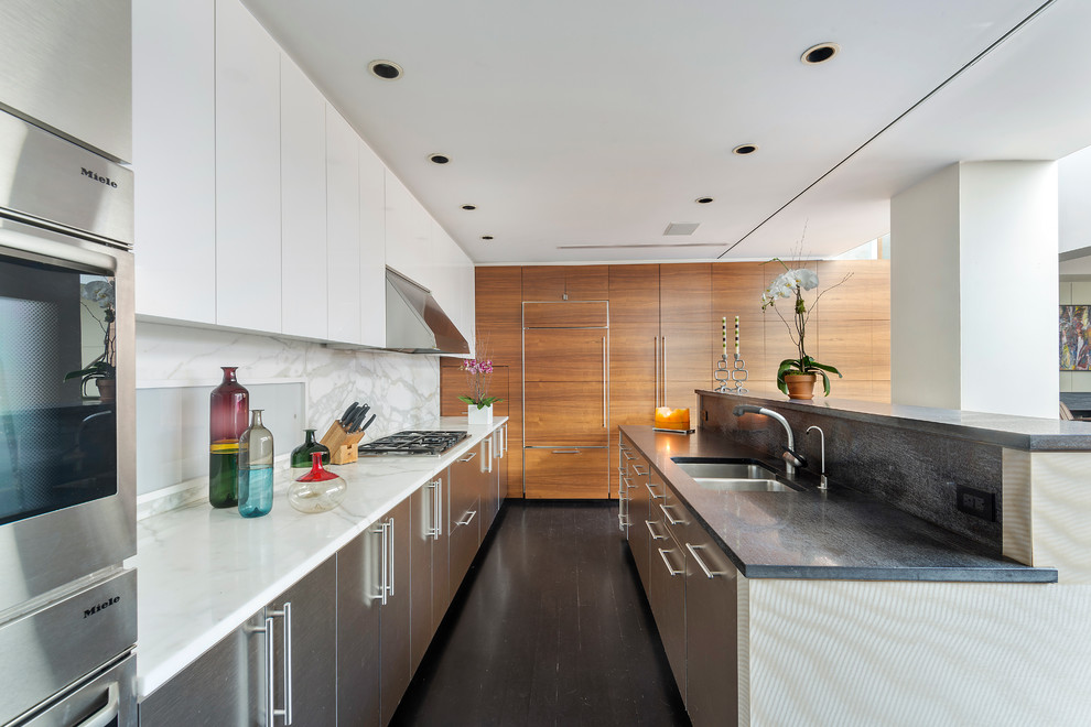 This is an example of a large contemporary galley kitchen in New York with flat-panel cabinets, white cabinets, marble worktops, white splashback, dark hardwood flooring, an island, a double-bowl sink and integrated appliances.